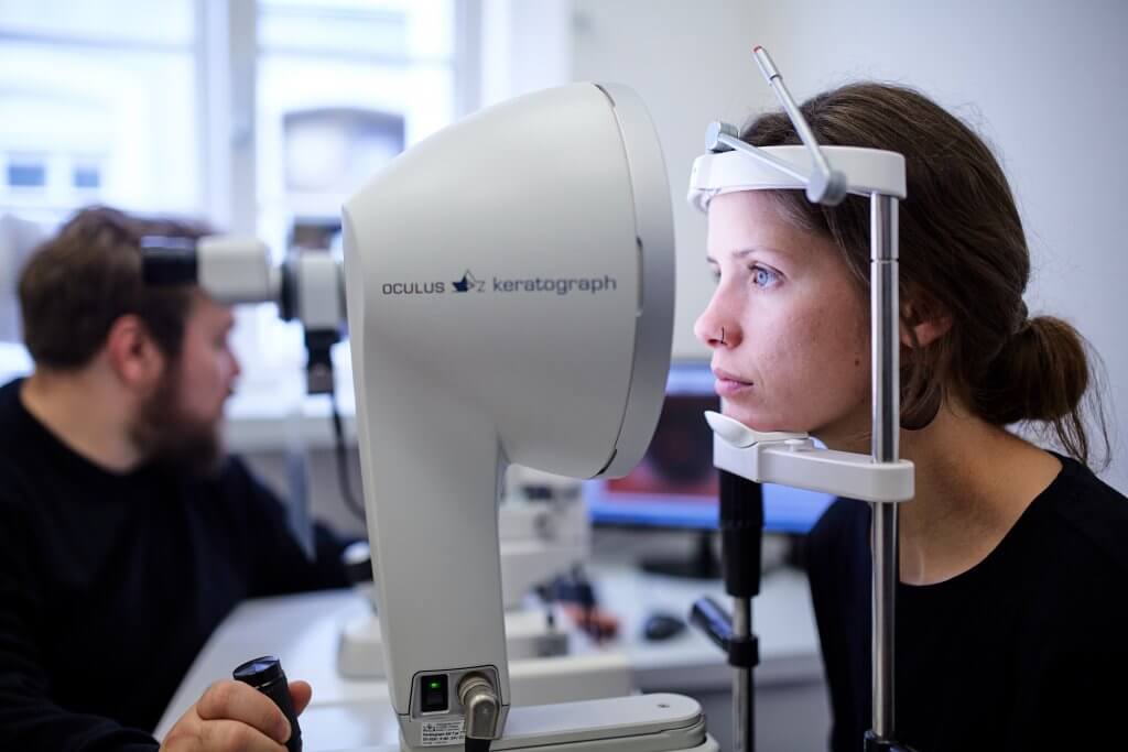 Eine Frau macht einen Gesundheits-Sehcheck mit einem Keratographen, während ein Mann das Gerät in einer Augenklinik bedient