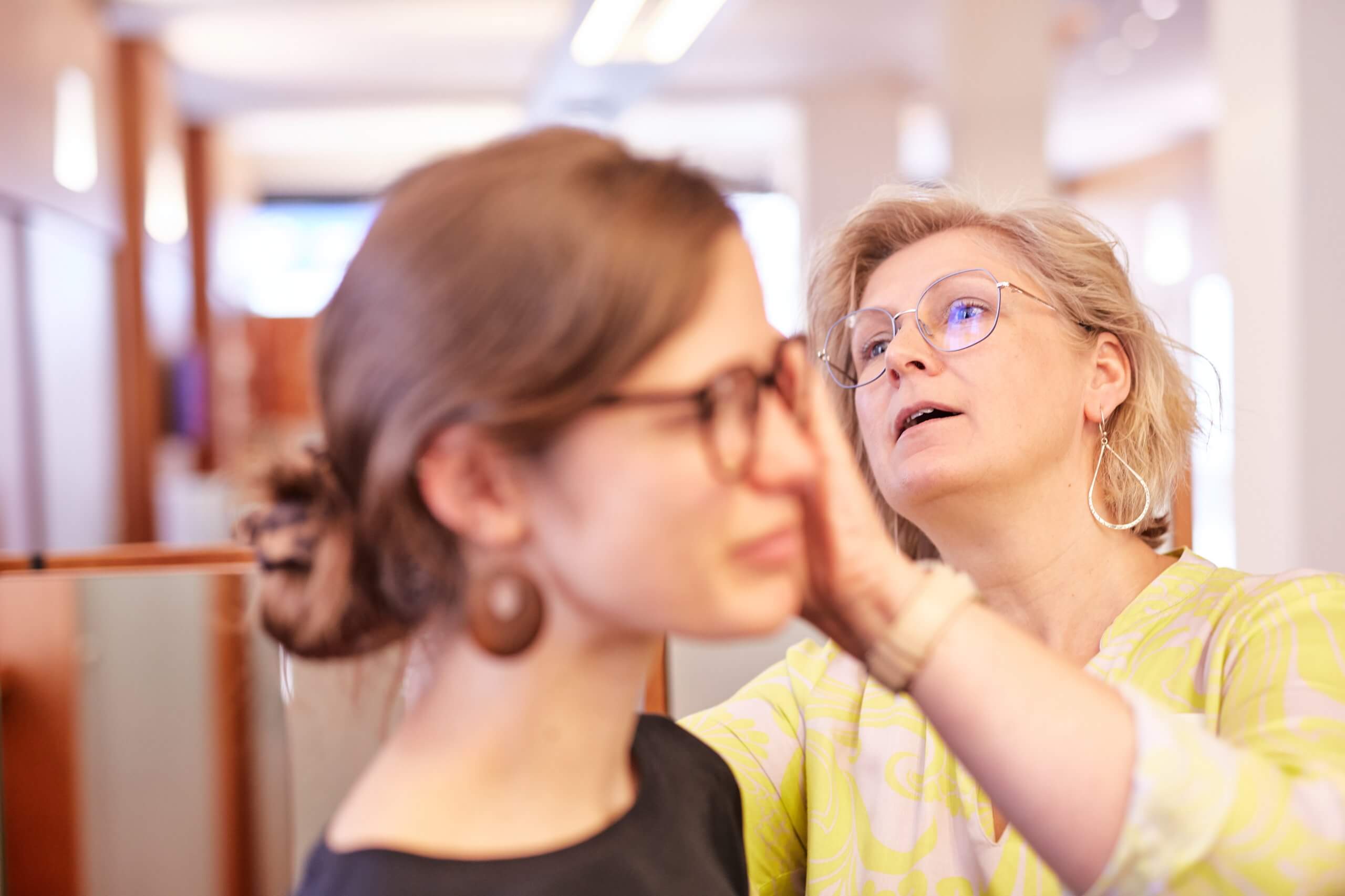 Eine Frau richtet einer anderen Frau die Brille in einem hellen, modernen Innenraum