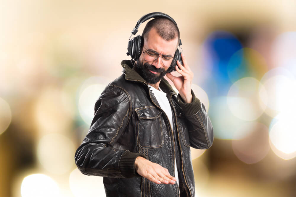 Ein Mann mit Kopfhörern und Lederjacke genießt Musik, hat die Augen geschlossen und wirkt wie ein DJ, pure Vibes