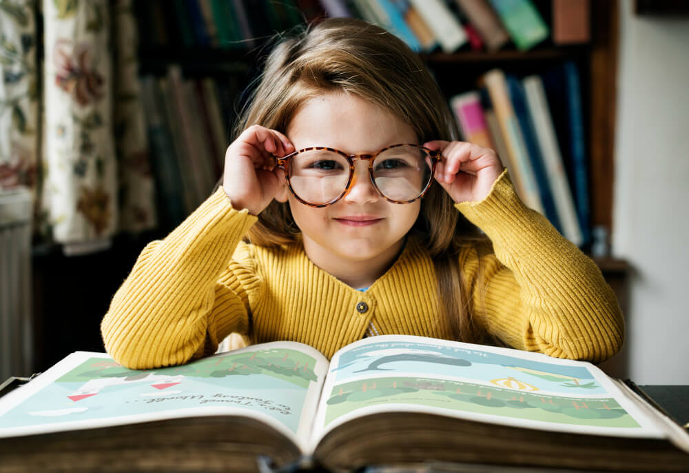 Ein lächelndes Kind mit Brille liest in einem Bilderbuch und trägt einen gelben Pullover, als würde es einen automatisch gespeicherten Entwurf entdecken
