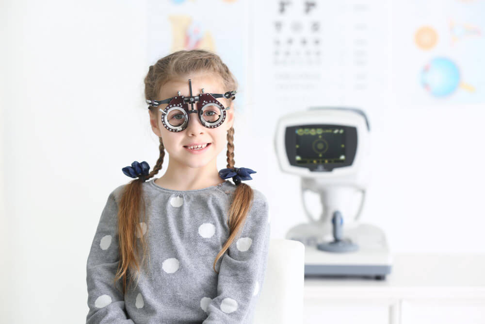 Ein lachendes Mädchen mit Zöpfen trägt Sehtest-Prüfbrillen in einer Augenklinik bei einer automatisch gespeicherten Sehprüfung