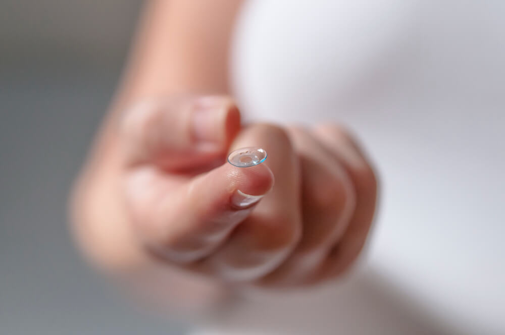 Eine Hand hält eine transparente Kontaktlinse auf der Fingerspitze, im Hintergrund ist alles unscharf wie bei einem automatisch gespeicherten Entwurf