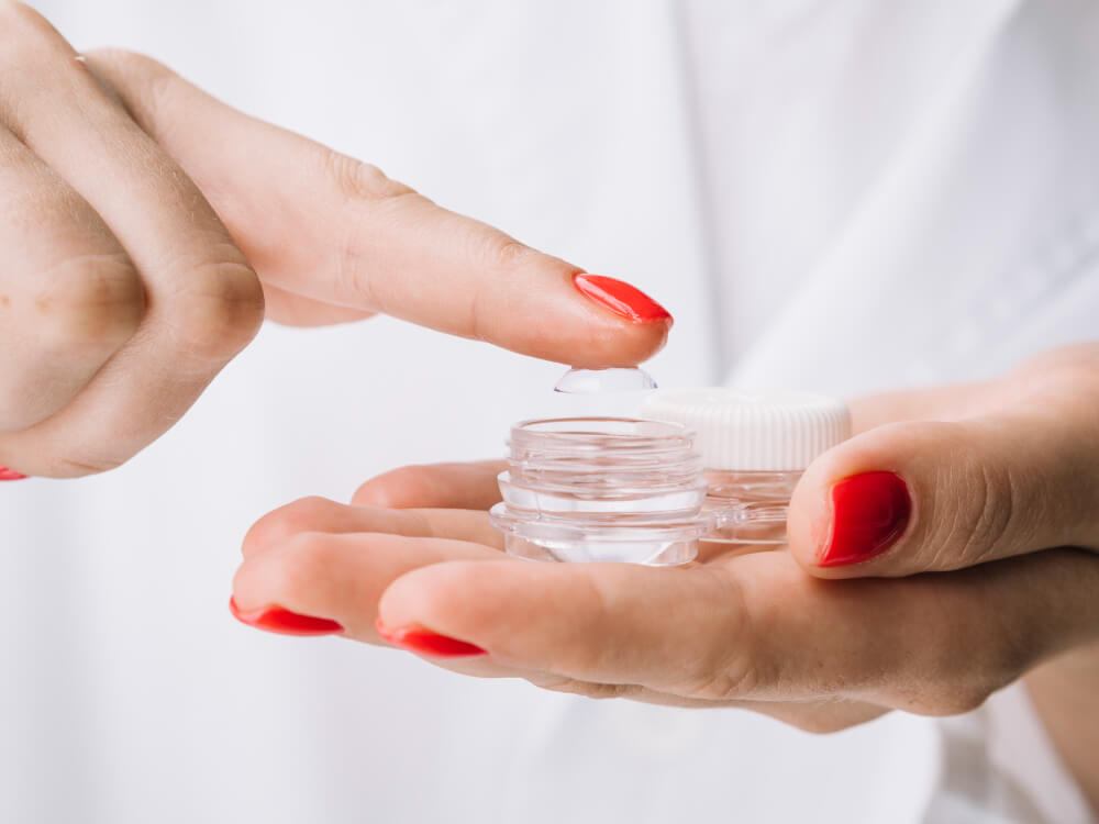 Eine Person mit rotem Nagellack nimmt eine Ortho-K-Linse auf, um sie nachts zu tragen und morgens scharf sehen zu können