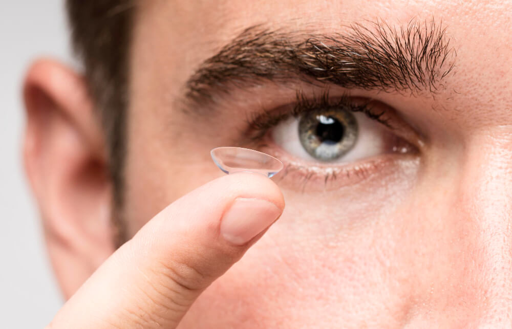 Eine Person hält eine Kontaktlinse nah ans Auge und setzt sie gleich ein, geeignet für Menschen mit trockenen Augen