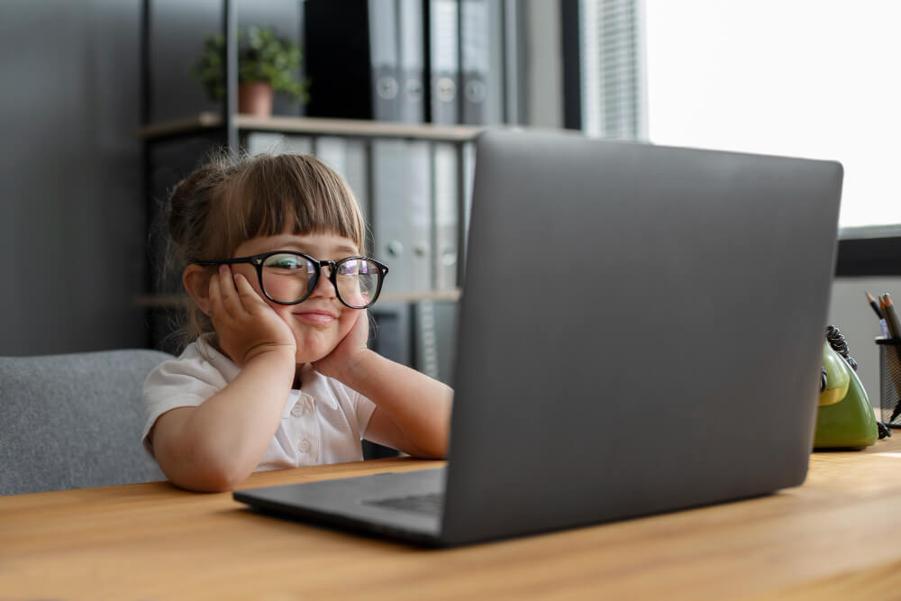 Ein Kind mit Brille sitzt lächelnd am Schreibtisch vor einem Laptop mit der Aufschrift "Automatisch gespeicherter Entwurf".